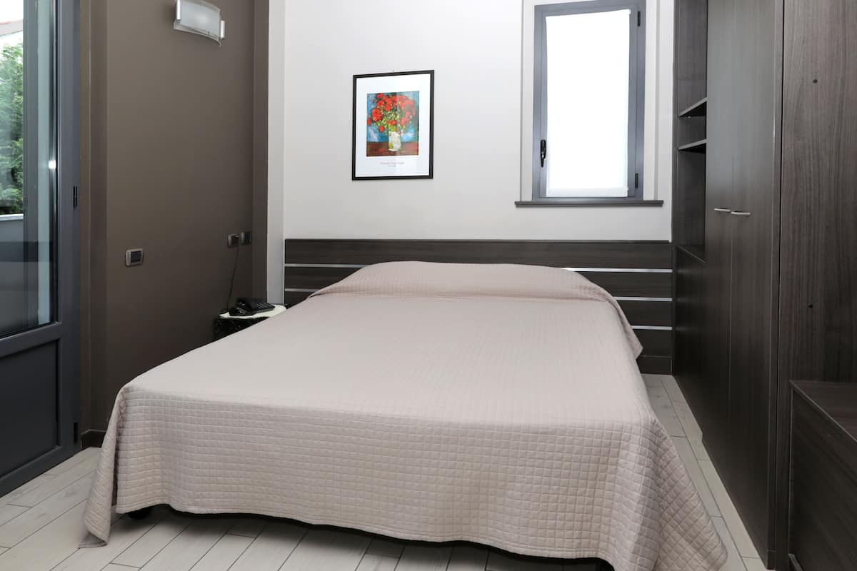 A bedroom with a bed, a nightstand, a framed picture on the wall, and a window.