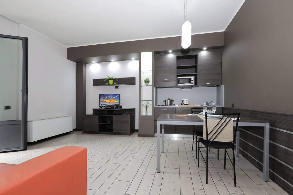 A modern kitchen with a dining area, a TV, and a sofa.