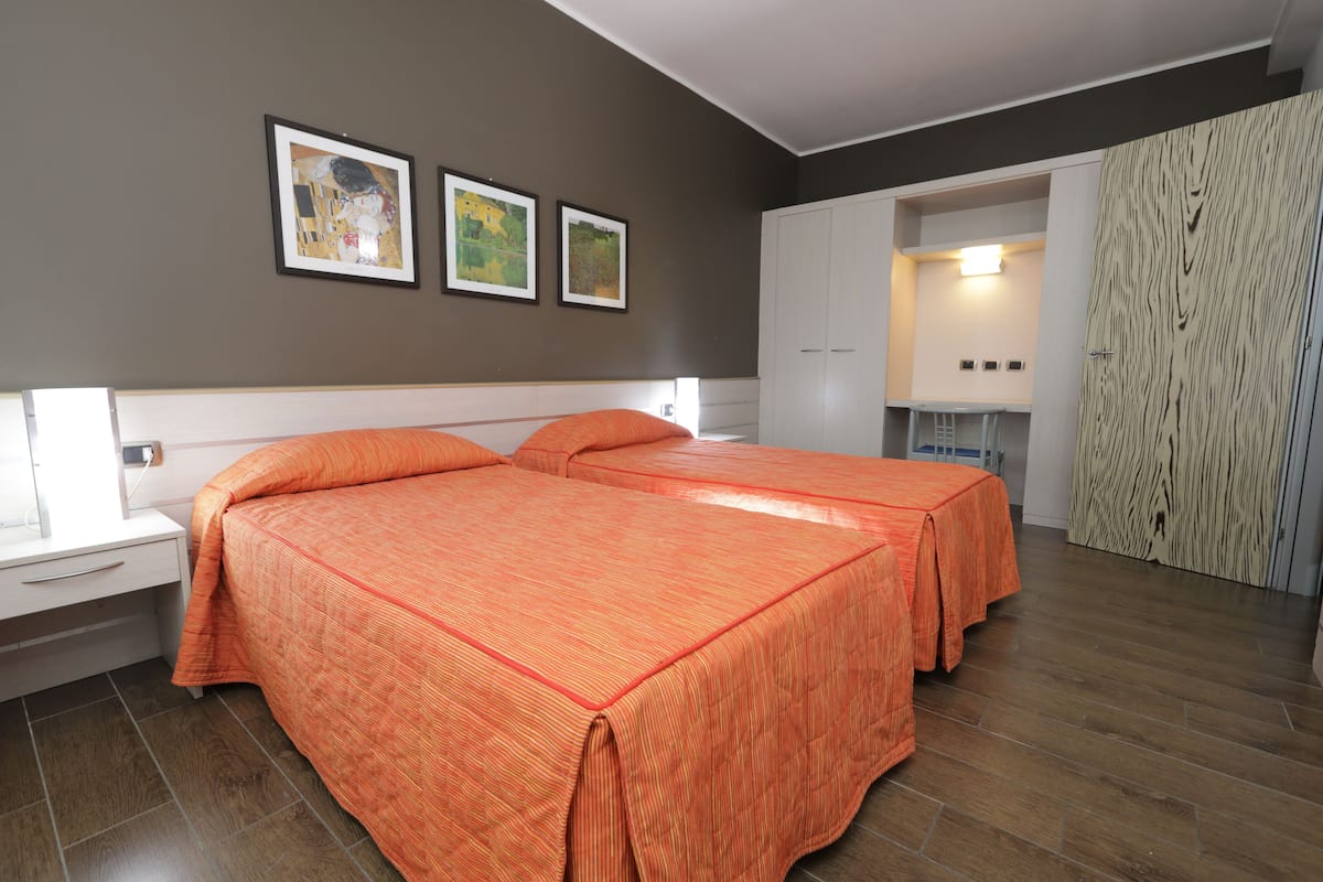 A modern bedroom with two beds, a wardrobe, and a bathroom visible through an open door.