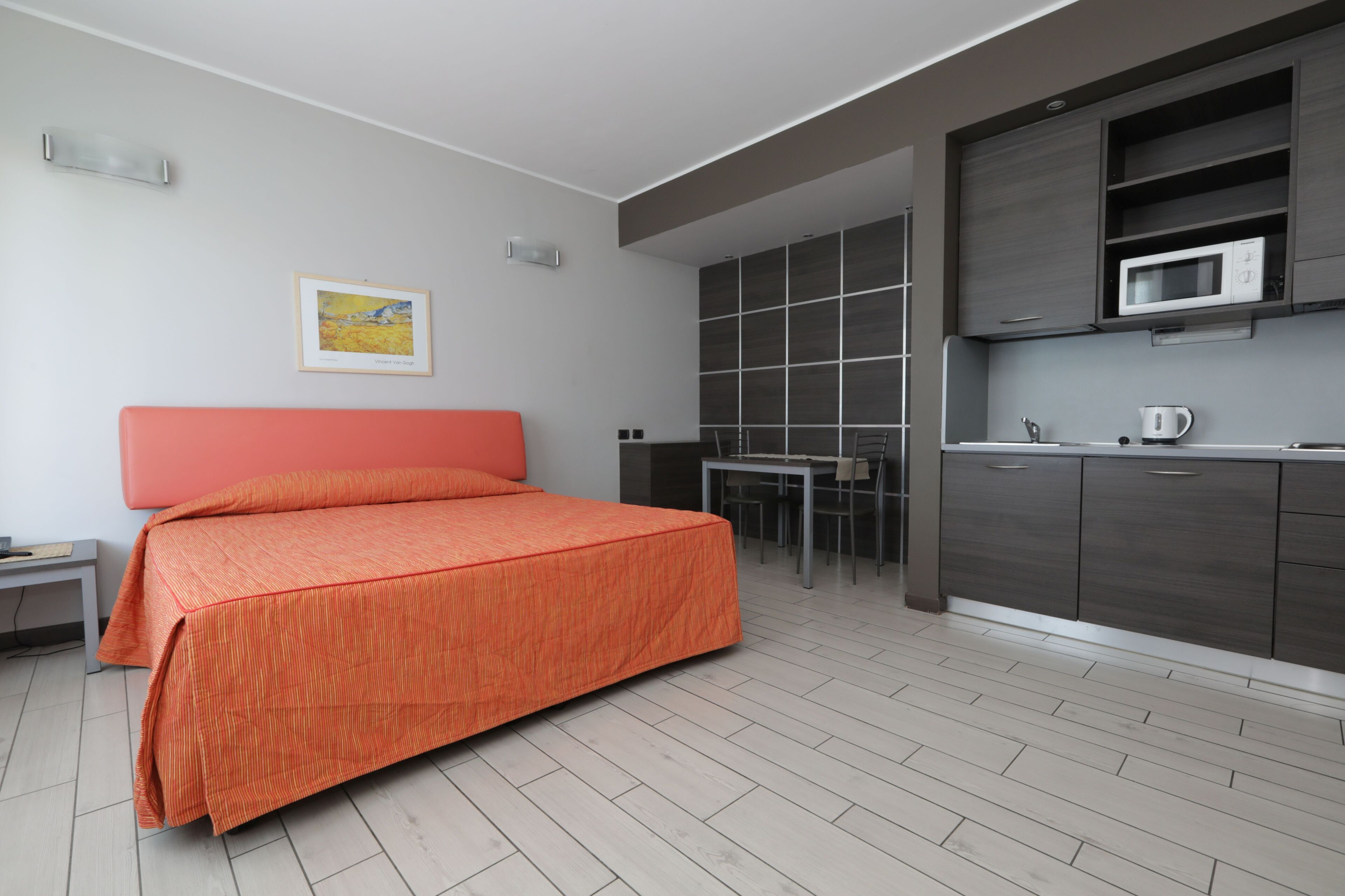 A modern bedroom with a bed, a desk, and a kitchenette.