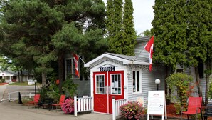 A small red and white building labeled "OFFICE" with a signboard indicating amenities like a gift shop, ice cream, and indoor heated pool. - Colonial Resort-1000 Islands (Gananoque)