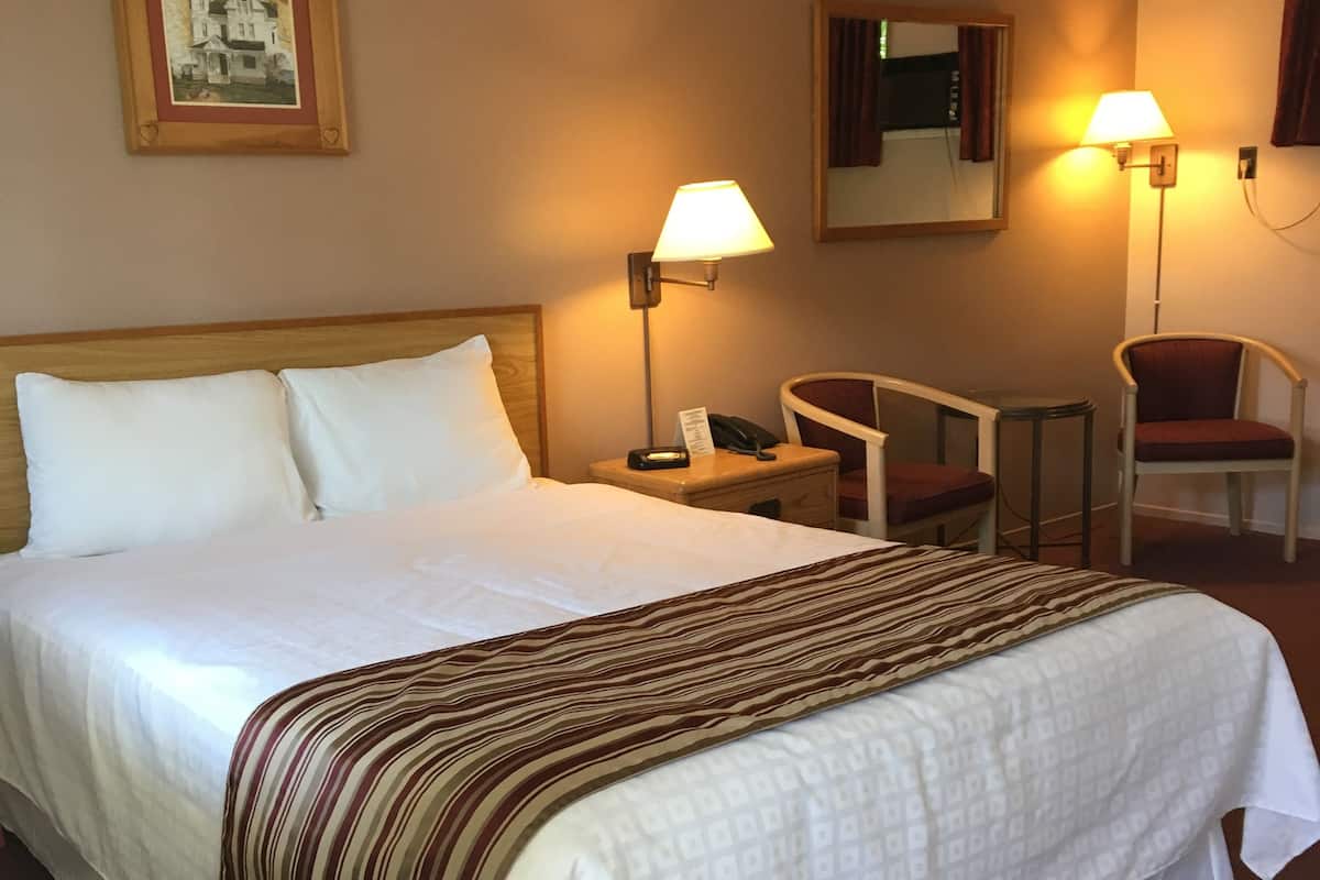 Une chambre d’hôtel avec un grand lit, deux lampes de chevet, une chaise, une petite table et un tableau encadré au mur.