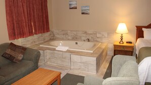 A hotel room with a large bathtub, a sofa, a chair, a bedside table, and a lamp. - Colonial Resort-1000 Islands (Gananoque)