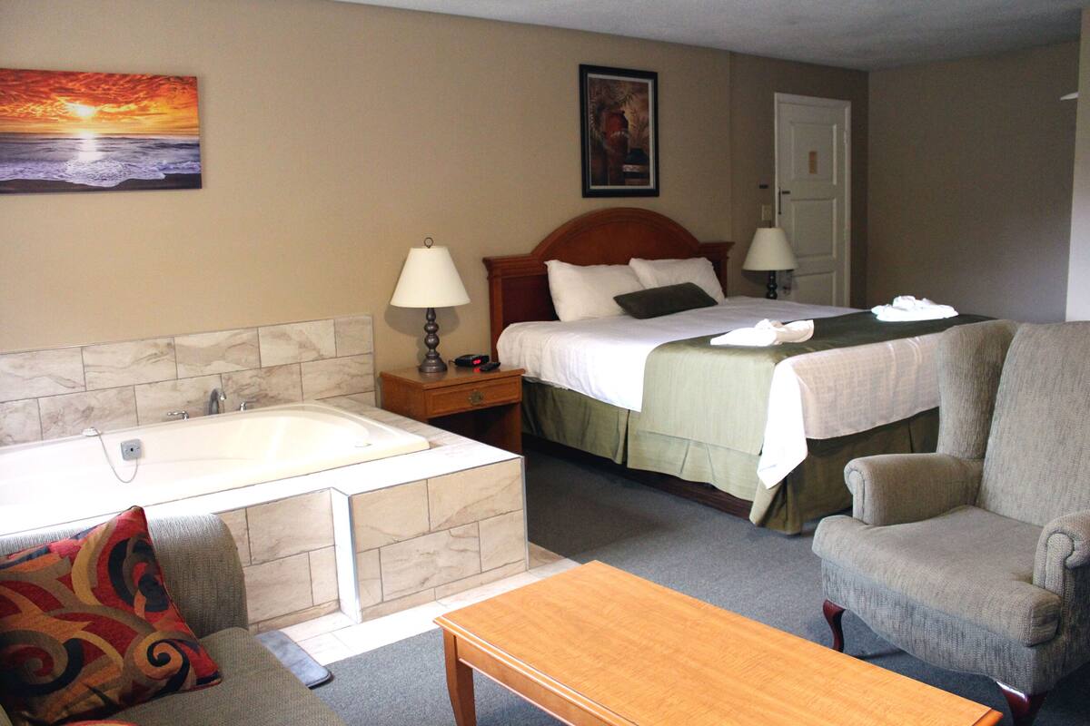 Une chambre d’hôtel avec un lit, une chaise, une table, une baignoire et un tableau au mur.