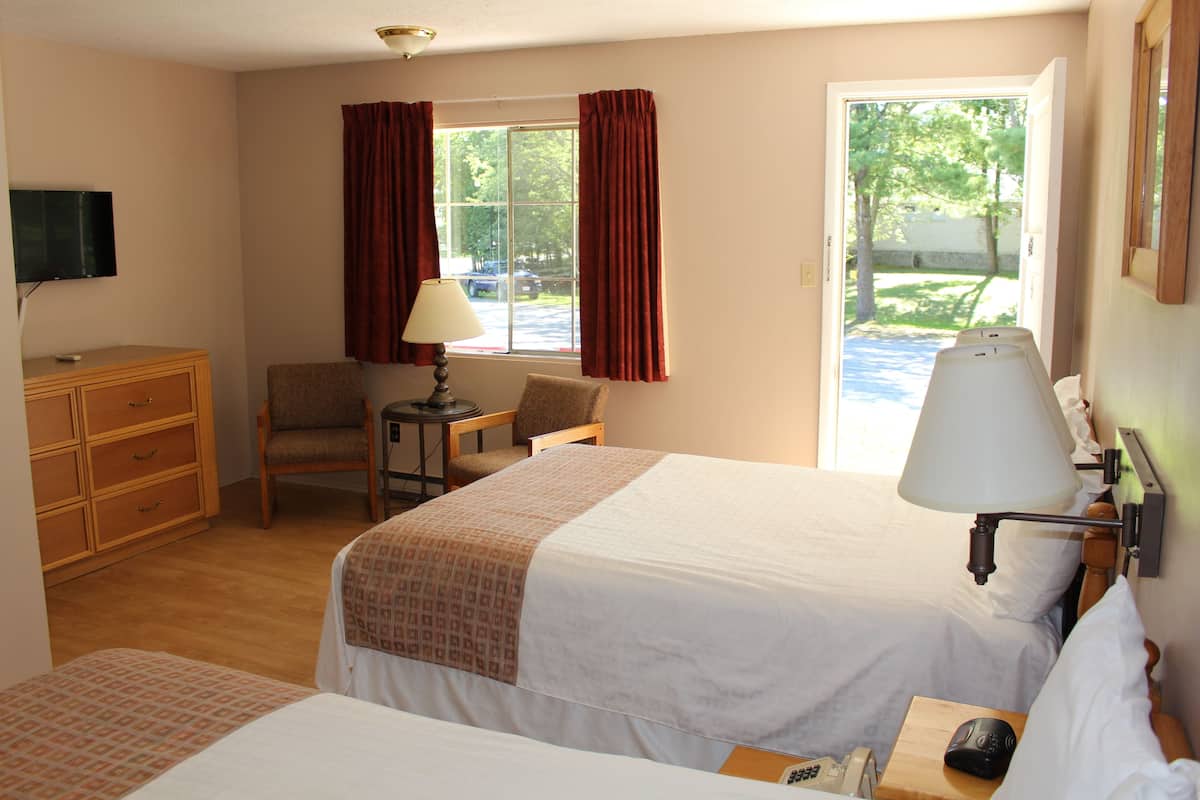 Une chambre d’hôtel avec deux lits, un bureau, une chaise, une télévision et une fenêtre avec des rideaux.