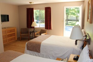 A hotel room with two beds, a desk, a chair, a TV, and a window with curtains. - Colonial Resort-1000 Islands (Gananoque)