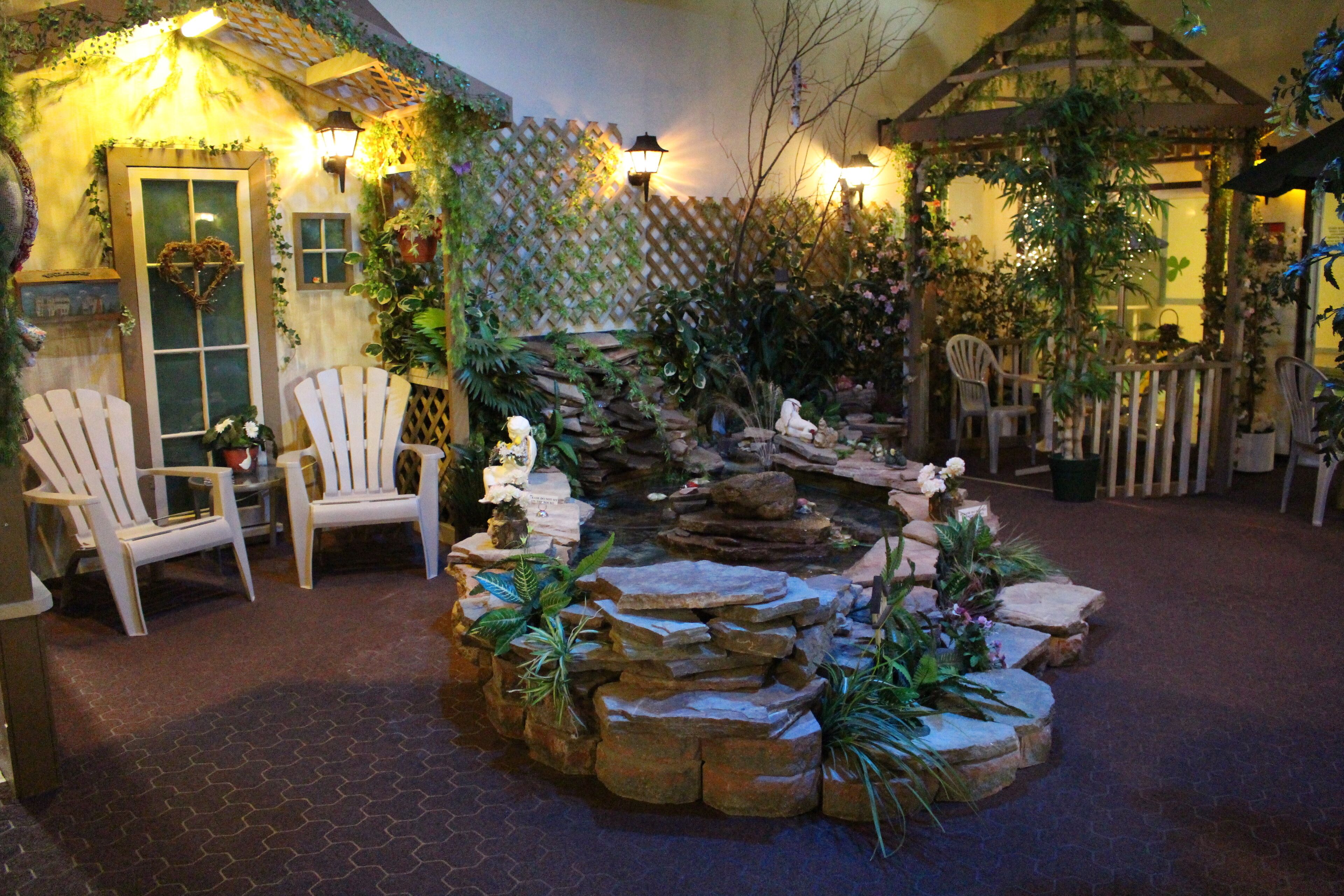Un jardin intérieur accueillant, avec un grand rocher au centre, des chaises blanches et une décoration en forme de cœur sur une porte.