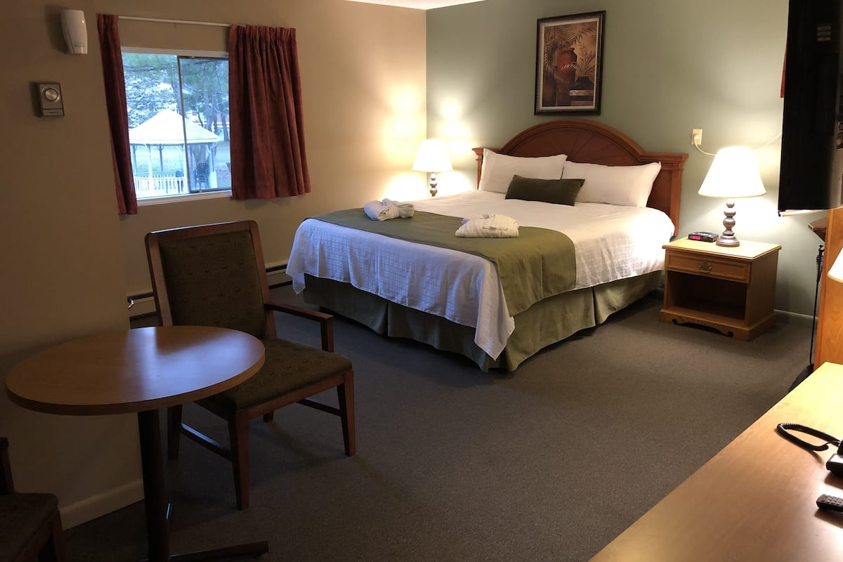 Une chambre d’hôtel comprenant un lit, deux tables de chevet, une chaise, une petite table et une fenêtre avec des rideaux.