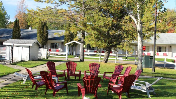 A grassy area with red Adirondack chairs arranged in a circle, a sign that reads "BOCE BALL," and a white building in the background. - Colonial Resort-1000 Islands (Gananoque)