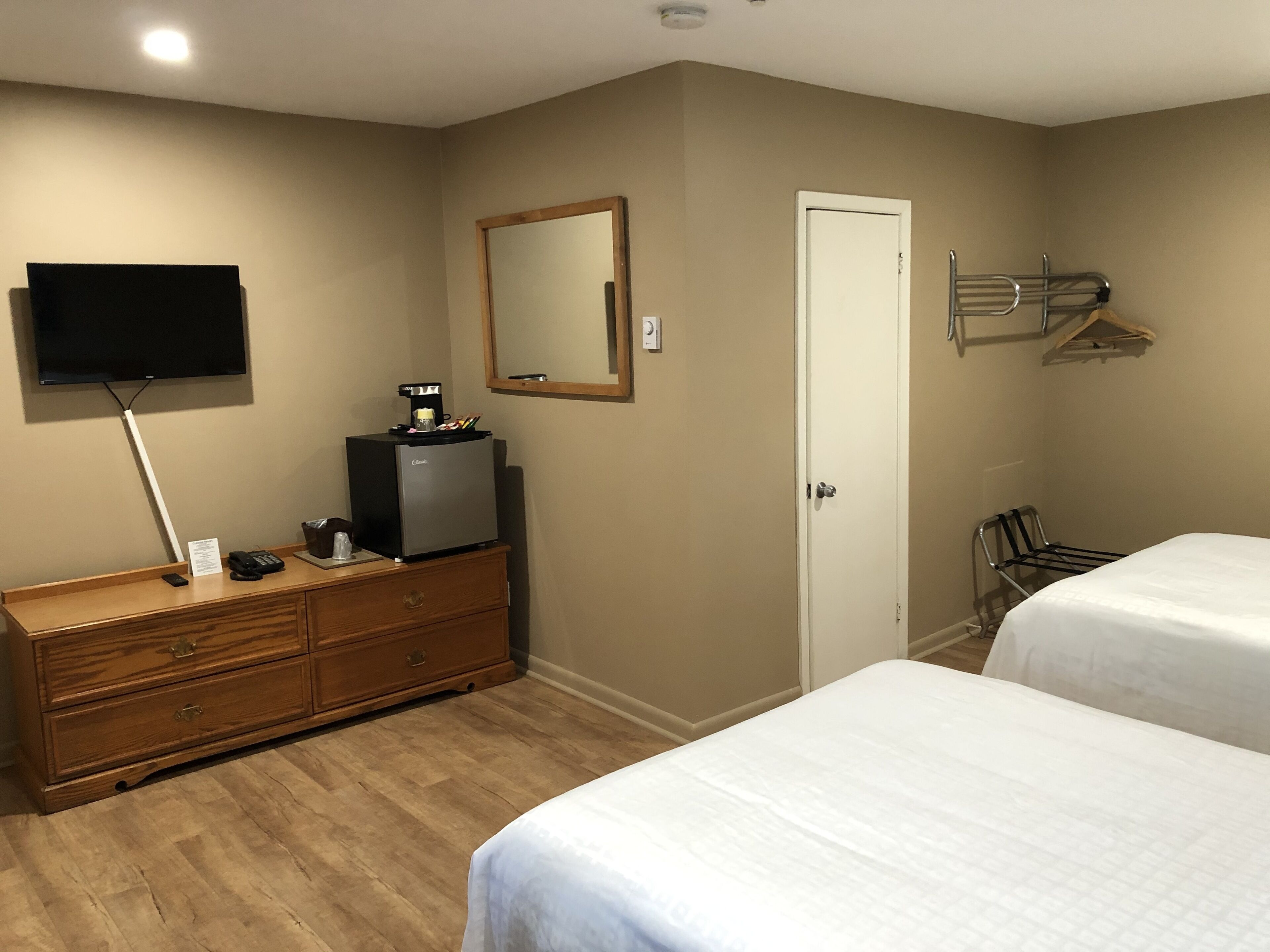 A hotel room with a wooden dresser, a flat-screen TV, a coffee maker, a mirror, a door, and two beds.