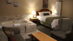 A hotel room with a bed, a sofa, a chair, a table, a bathtub, and a door. - Colonial Resort-1000 Islands (Gananoque)