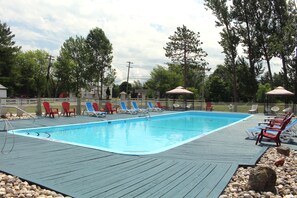 A swimming pool with lounge chairs and umbrellas, surrounded by trees and a wooden deck. - Colonial Resort-1000 Islands (Gananoque)