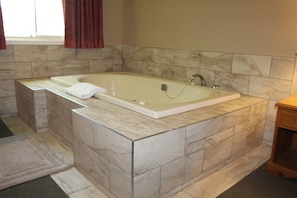 A bathroom with a large bathtub, marble tiles, and a wooden cabinet.