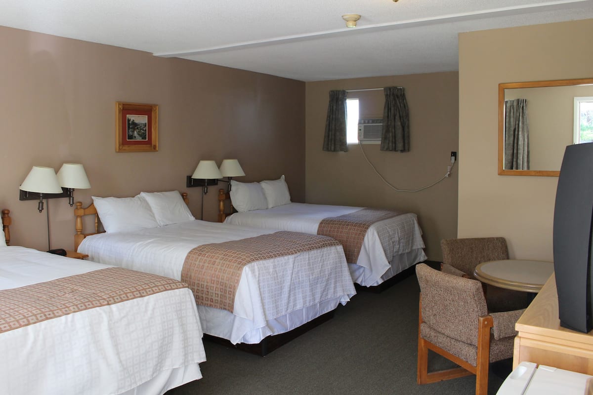 Une chambre d’hôtel avec trois lits simples, un bureau avec une chaise, une télévision et un cadre avec une image accroché au mur.