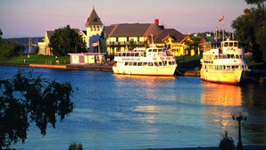A waterfront hotel with two boats docked, a lawn, and a row of chairs. - Colonial Resort-1000 Islands (Gananoque)