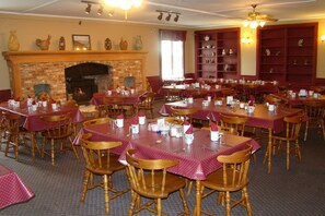 A dining area with multiple tables and chairs, a fireplace, and shelves with decorative items. - Colonial Resort-1000 Islands (Gananoque)