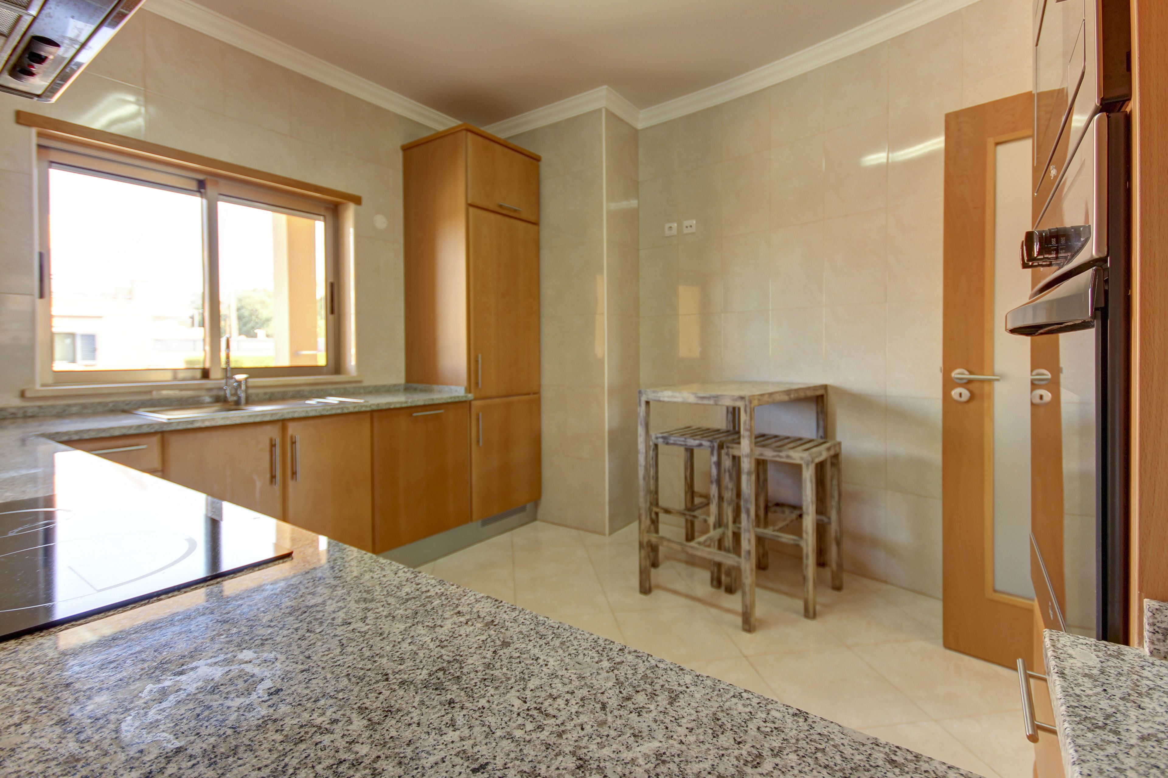 Une cuisine dotée de plans de travail en granit, de meubles en bois, d’une fenêtre et d’une porte.