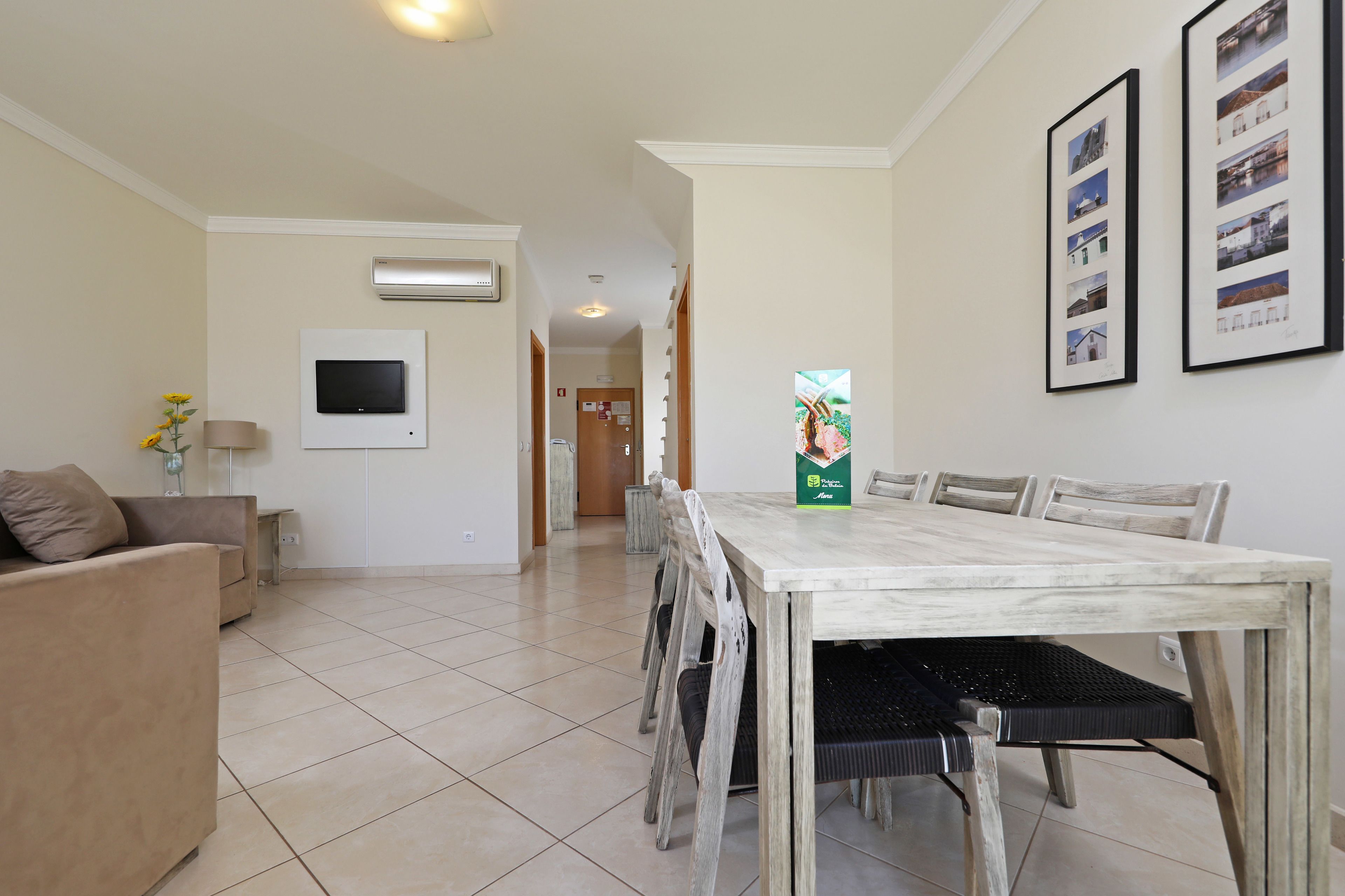 Een eetruimte met een grote tafel, stoelen, een televisie en ingelijste foto's aan de muur.
