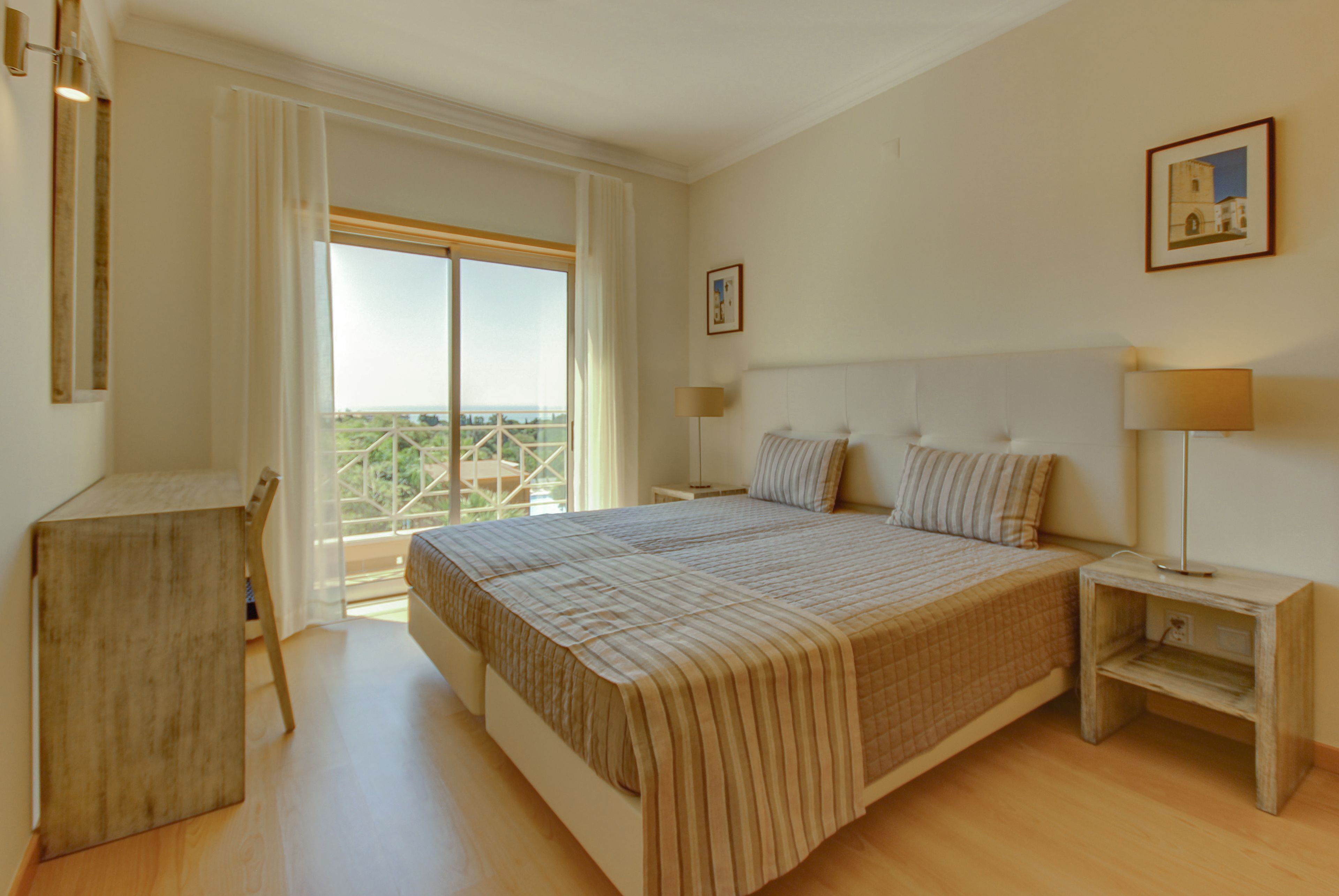 Une chambre à coucher avec un grand lit, un bureau, une chaise, une table de chevet et une fenêtre donnant sur un beau paysage.
