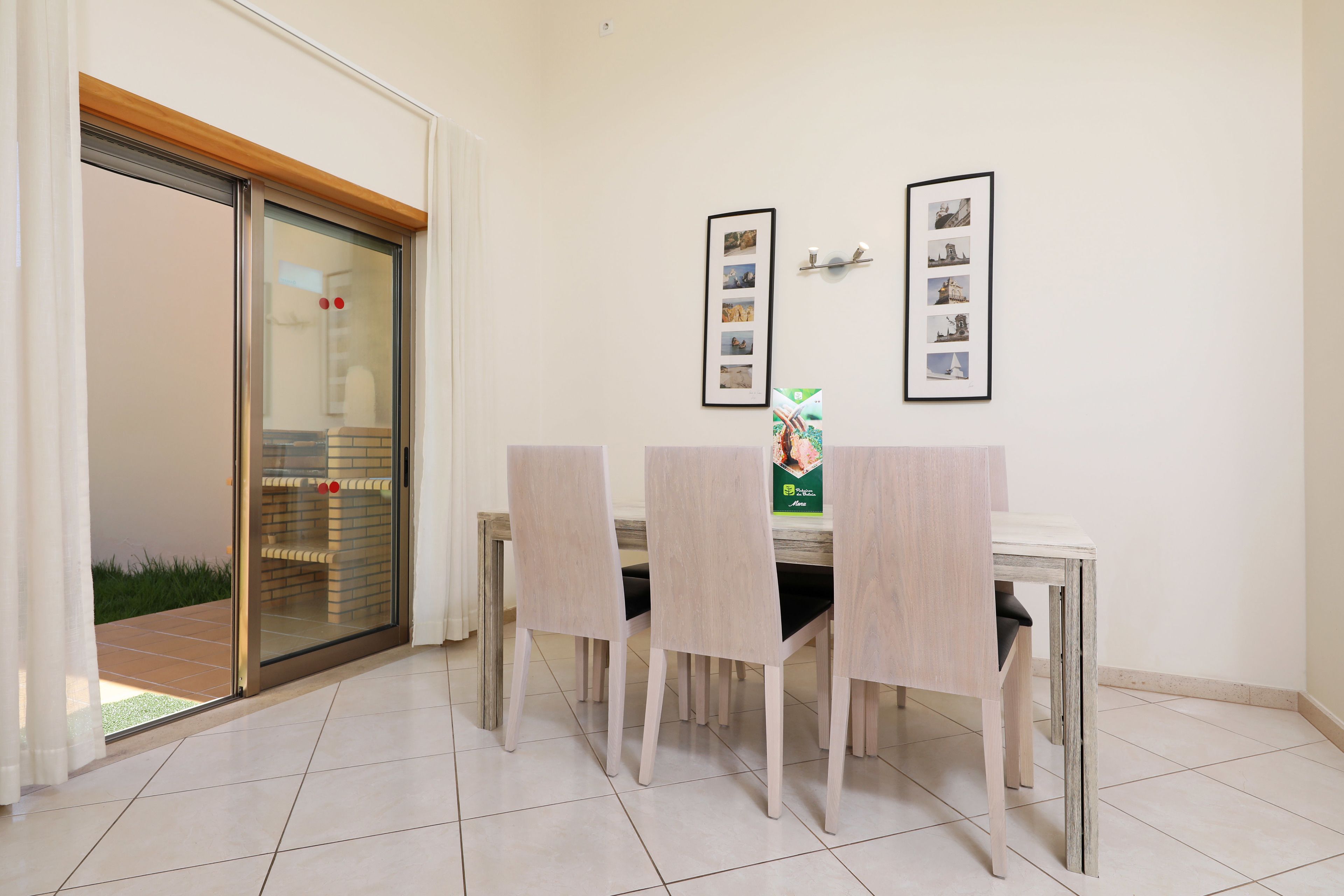 A dining area with a table and chairs, a glass door leading outside, and framed pictures on the wall.