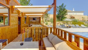 Um deck de madeira com sofá e mesa, com vista para uma piscina e espreguiçadeiras.