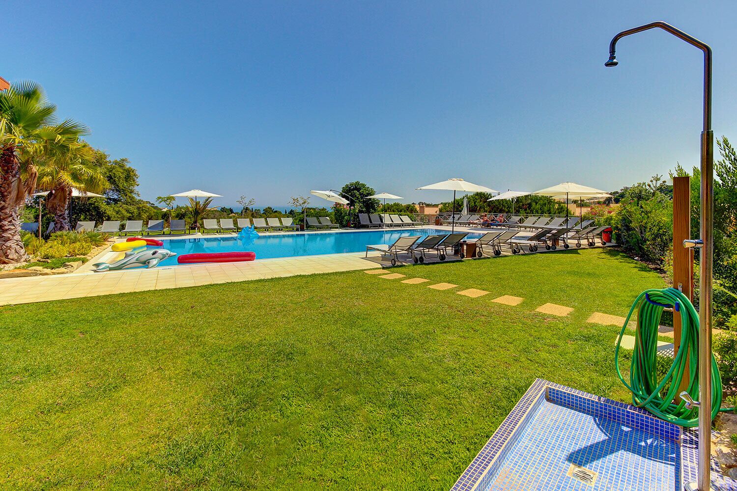 A swimming pool with lounge chairs and umbrellas, surrounded by a well-maintained lawn and palm trees.