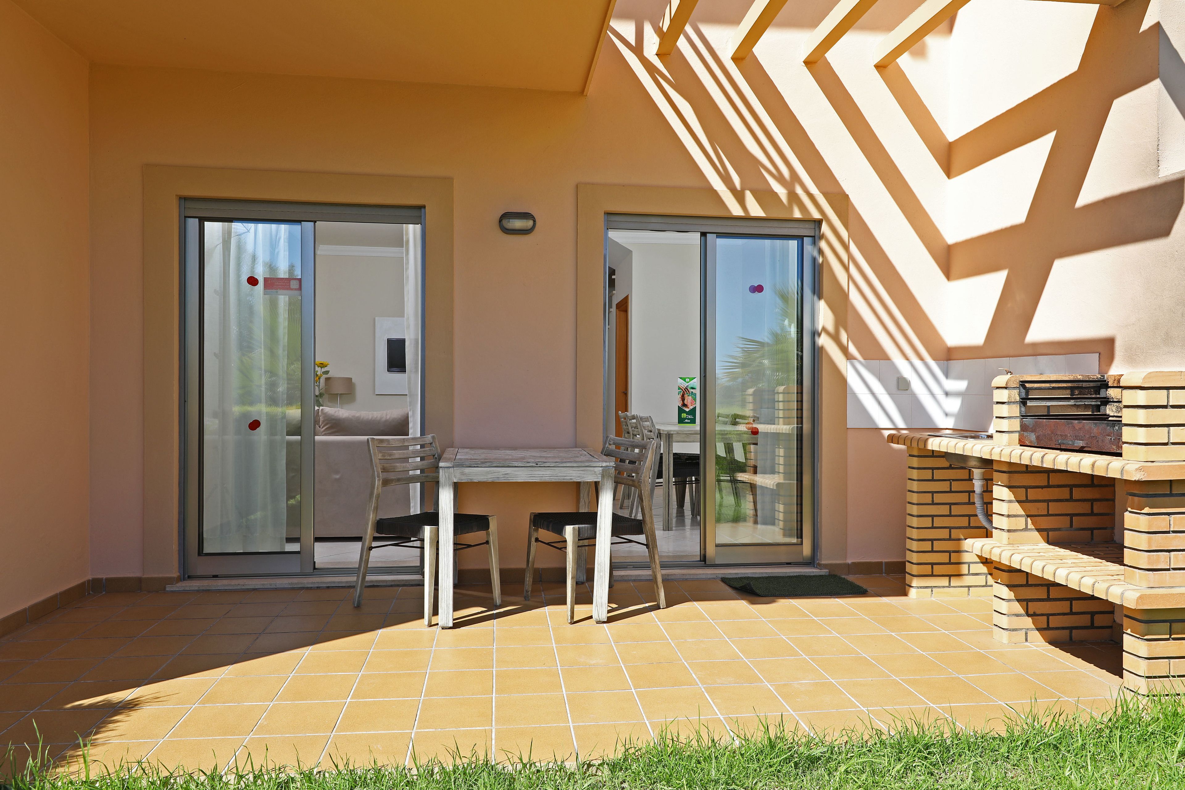 An outdoor patio with a table and chairs, a brick barbecue, and sliding glass doors leading to a balcony.