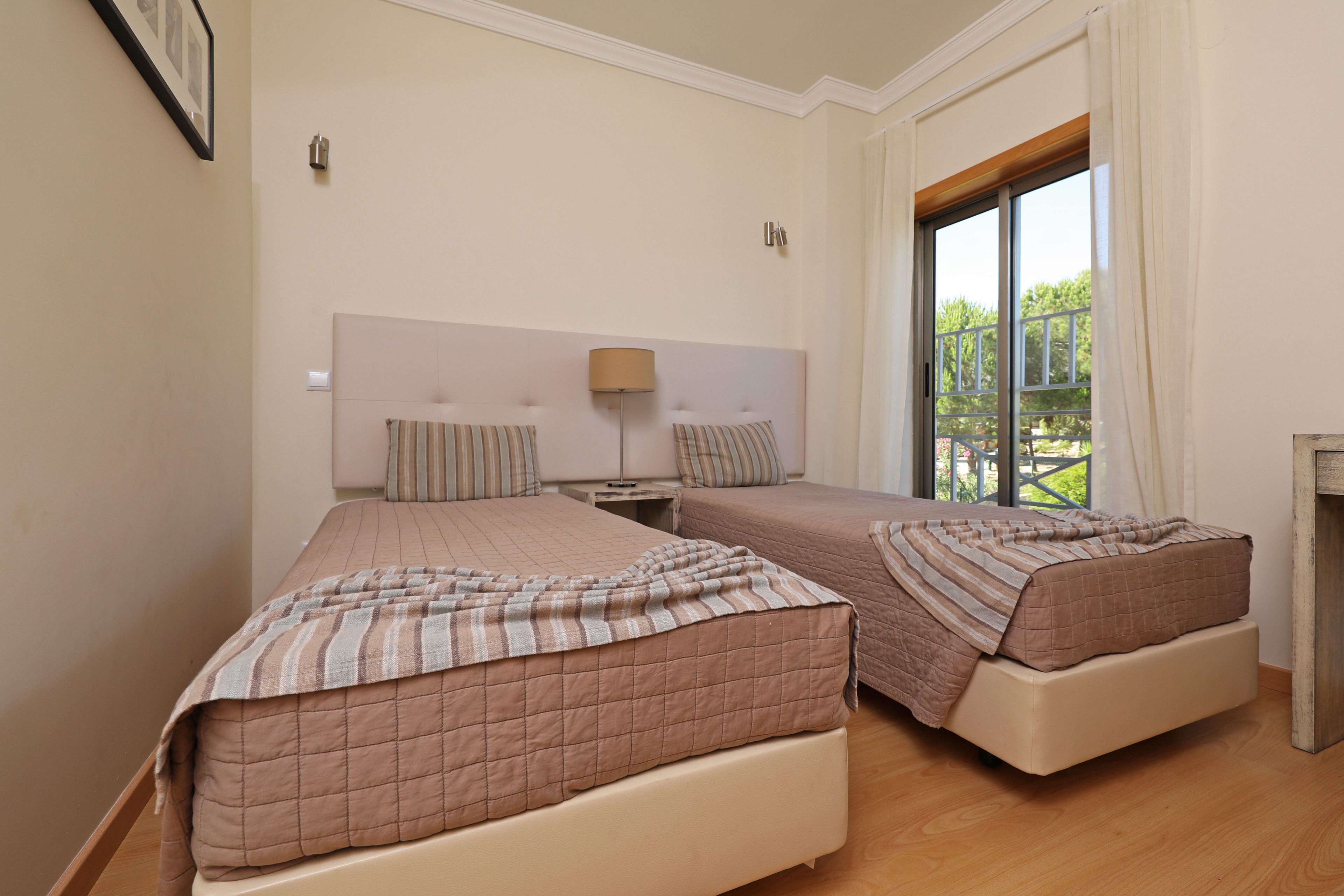 A bedroom with two beds, a nightstand, a lamp, and a window with curtains.