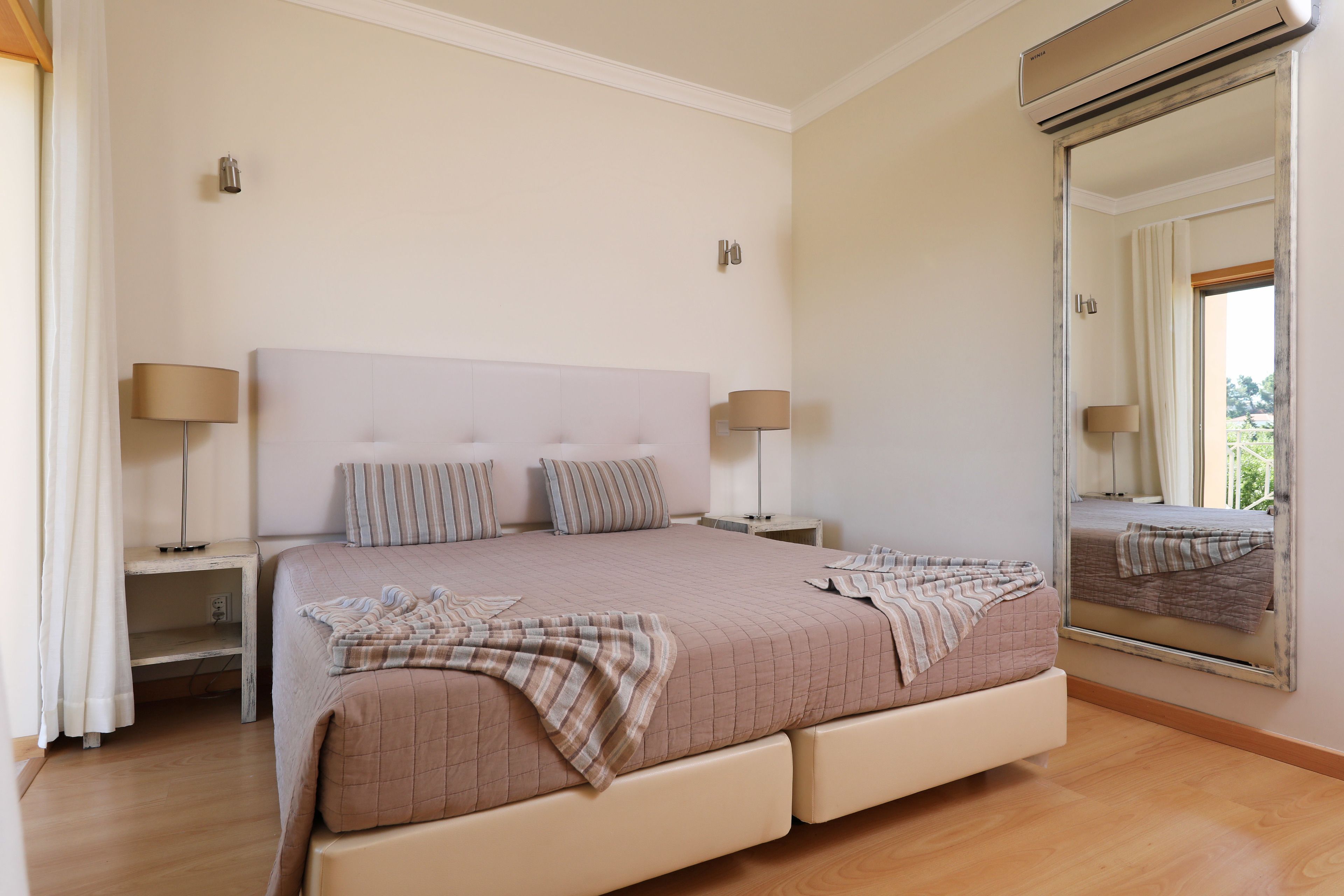 A bedroom with a large bed, two bedside tables, a mirror, and a ceiling fan.