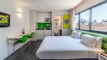 A hotel room with a bed, a desk, a chair, a small kitchenette, and a bathroom.