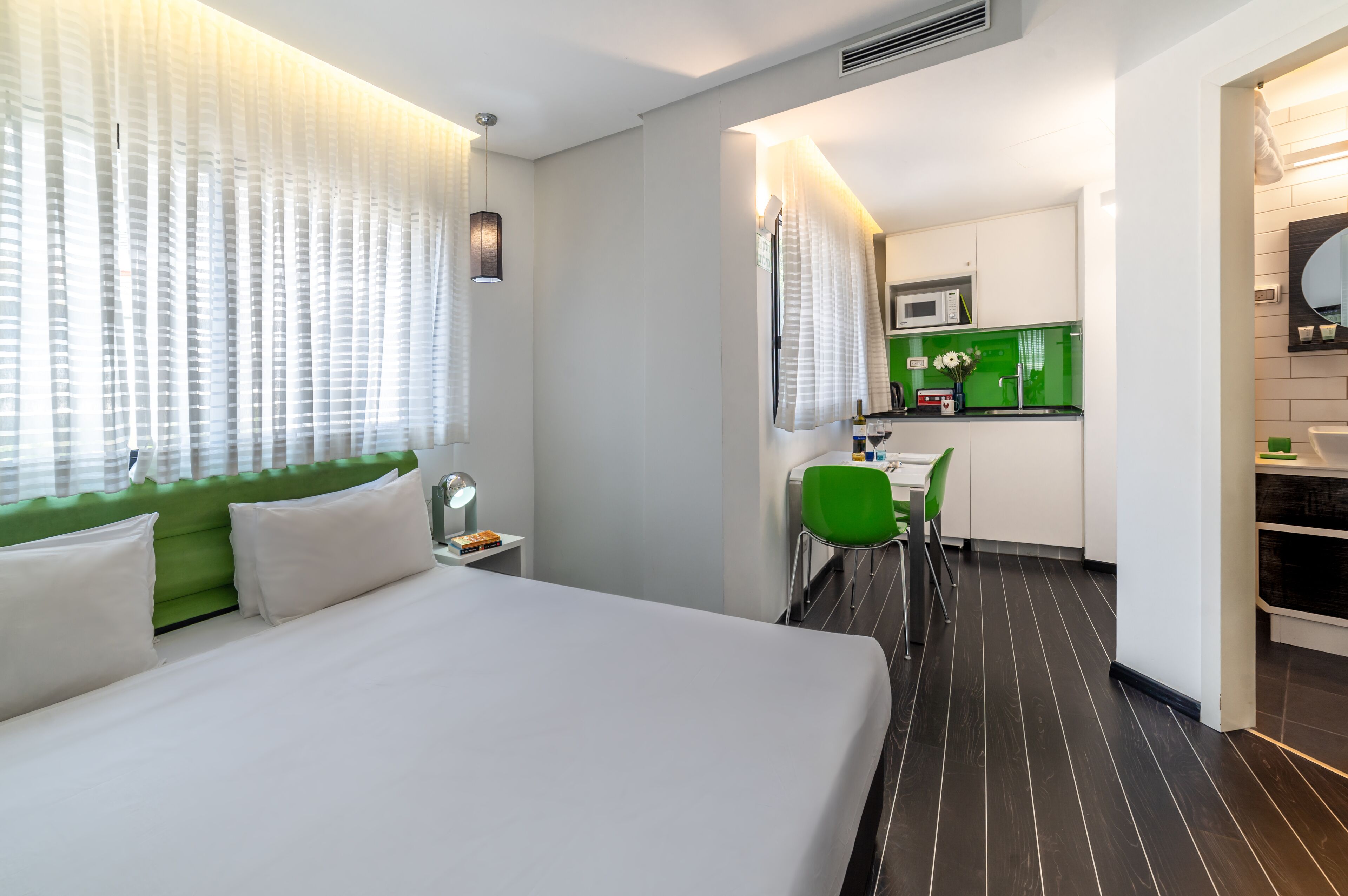 Habitación de hotel con cama, escritorio, silla, kitchenette y baño.