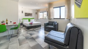 A modern hotel room with a bed, a desk, a chair, a sofa, and a large window with curtains. - 130 Rock Apartments (Tel Aviv)