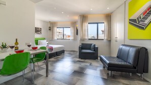 A modern living room with a dining area, a sofa, a chair, and a bed. - 130 Rock Apartments (Tel Aviv)