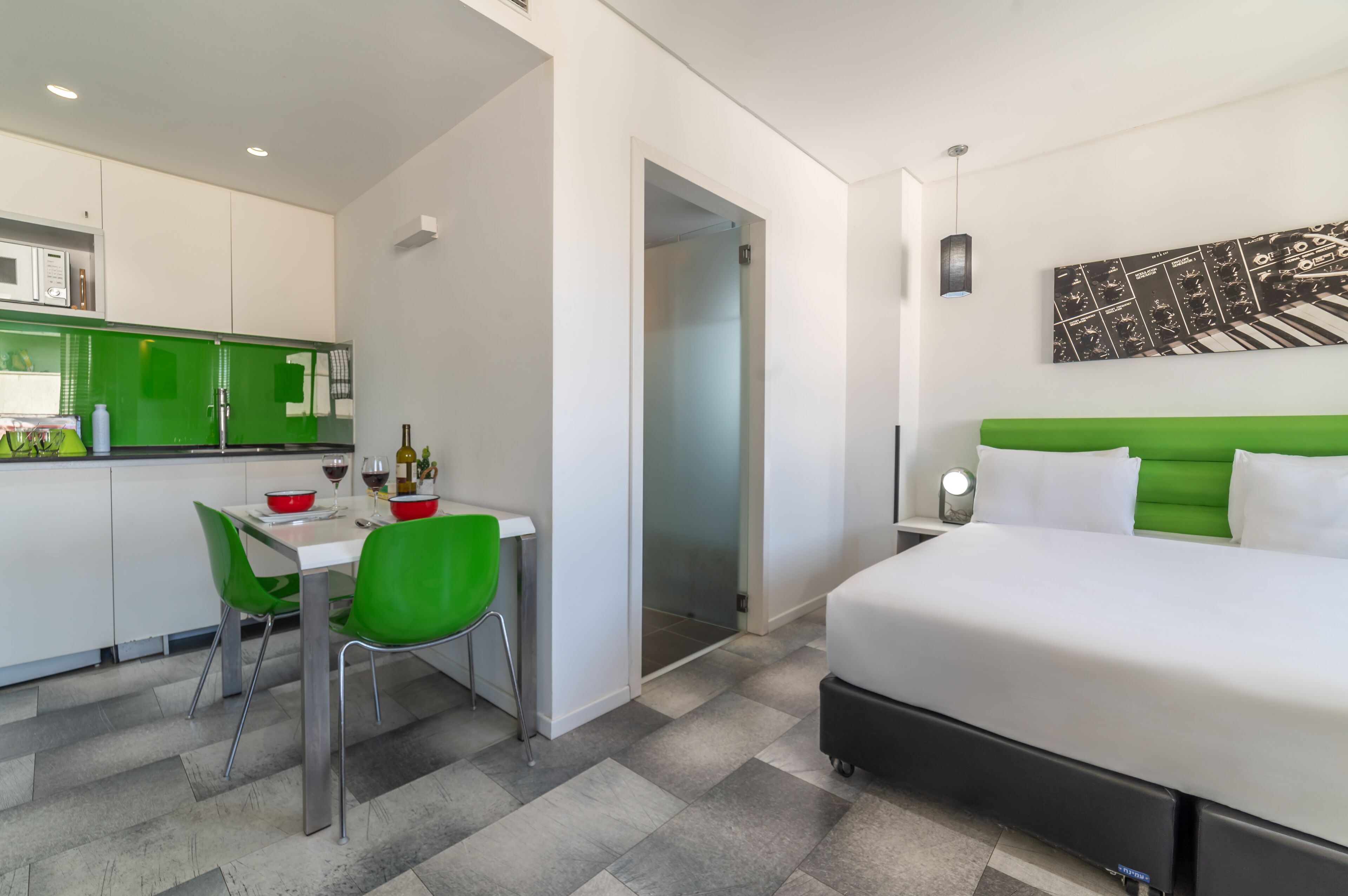 Une chambre d’hôtel moderne équipée d’un lit, d’un bureau avec une chaise, d’une kitchenette et d’une salle de bain.