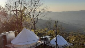 A campsite with two tents set up on elevated platforms, surrounded by trees and a view of distant hills. - Phu Mok Dok Mai Resort (Wiang Kaen)