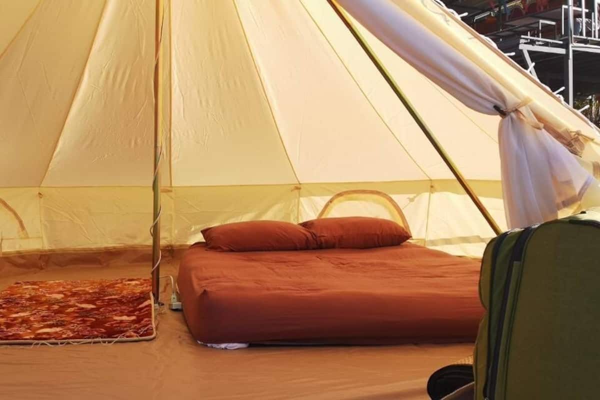 A tent with a bed, pillows, a blanket, and a small table with items.
