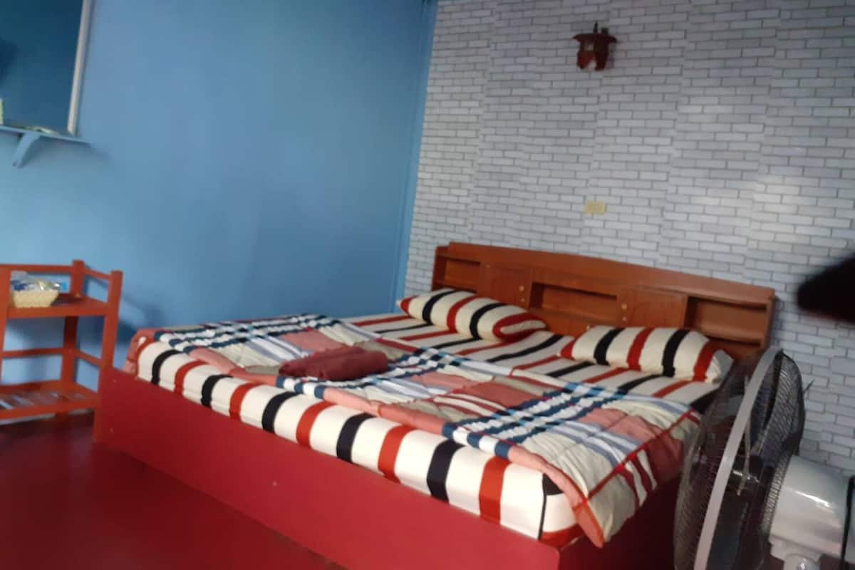 A bedroom with a wooden bed, a red chair, a white brick wall, and a small table.