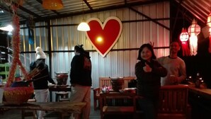 A rustic dining area with wooden tables and chairs, a large heart-shaped decoration, and a person giving a thumbs-up. - Phu Mok Dok Mai Resort (Wiang Kaen)