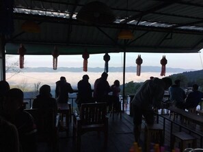 A covered outdoor seating area with tables and chairs, overlooking a mountainous landscape.
