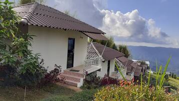 A row of white buildings with brown tiled roofs, a staircase leading to a balcony, and a view of mountains in the background.