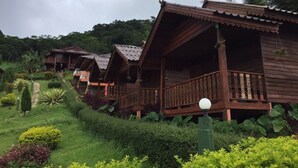 A row of wooden cabins with balconies, surrounded by lush greenery and a pathway. - Phu Mok Dok Mai Resort (Wiang Kaen)