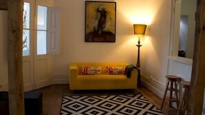 A yellow sofa with colorful pillows, a black and white patterned rug, a painting on the wall, and a lamp. - WW Hostel & Suites (Coimbra)