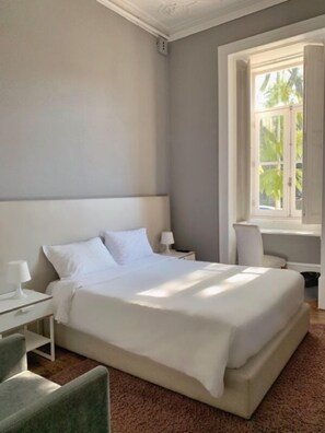 Une chambre avec un grand lit, une table de chevet, une chaise et une fenêtre donnant sur un paysage verdoyant.