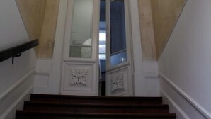 A grand staircase with a white balustrade, a large circular ceiling light, and a decorative door with glass panels. - WW Hostel & Suites (Coimbra)