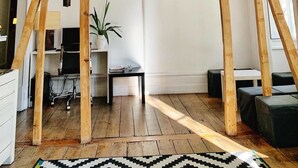 A room with exposed wooden beams, a flat-screen TV mounted on the wall, a potted plant, a small table, and a black and white rug on the floor. - WW Hostel & Suites (Coimbra)