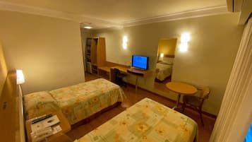 Una habitación de hotel con dos camas, un escritorio con ordenador, una mesita pequeña y una silla.