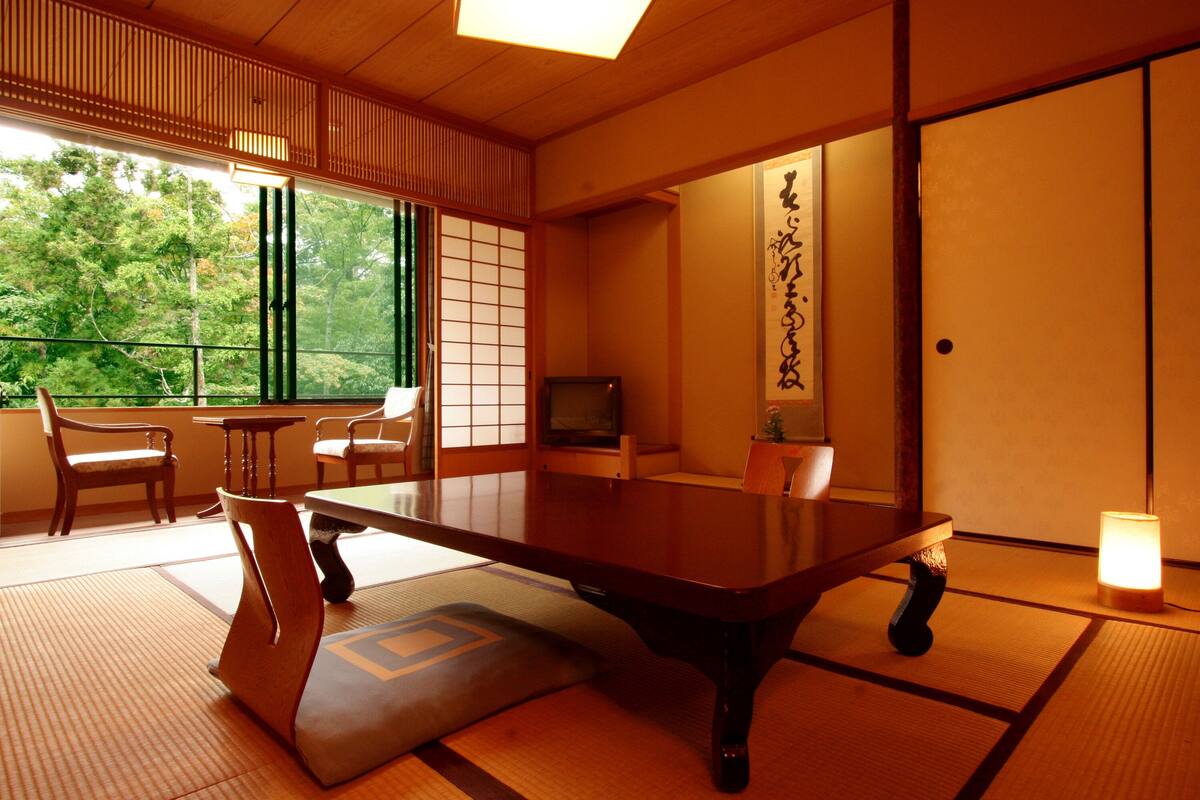 A traditional Japanese room with tatami flooring, a low table, chairs, a television, and a sliding door.