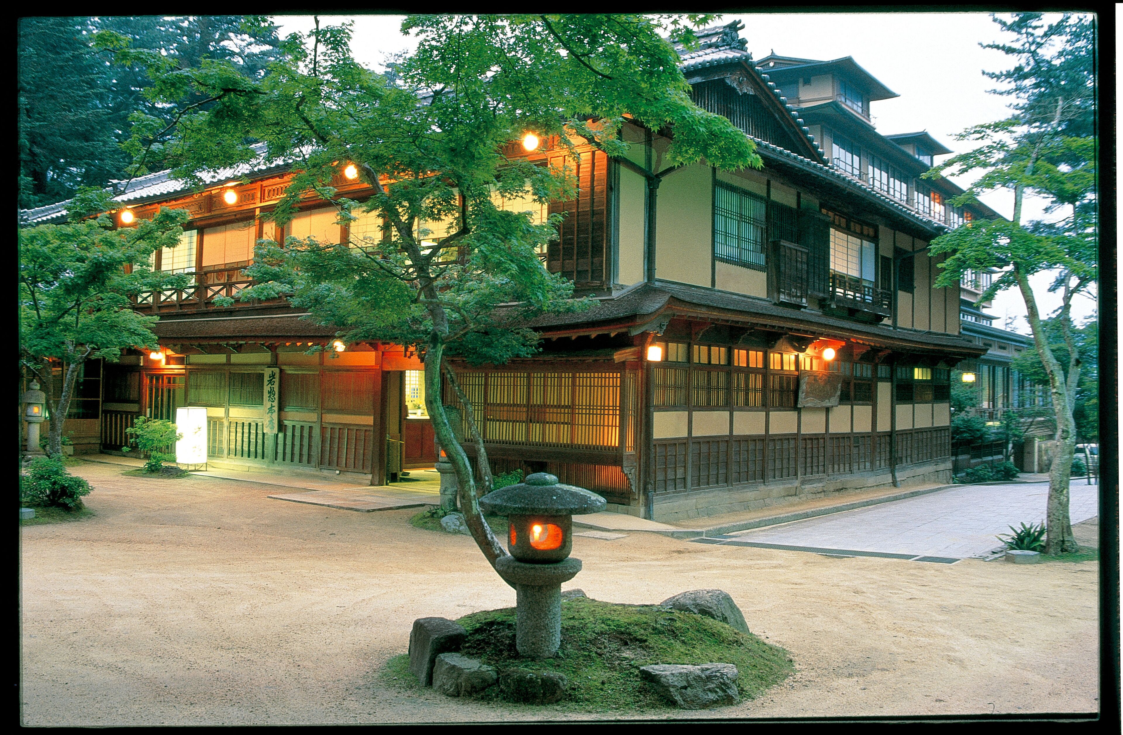 Un bâtiment traditionnel japonais, avec une façade en bois, de grandes fenêtres et une lanterne en pierre au premier plan.