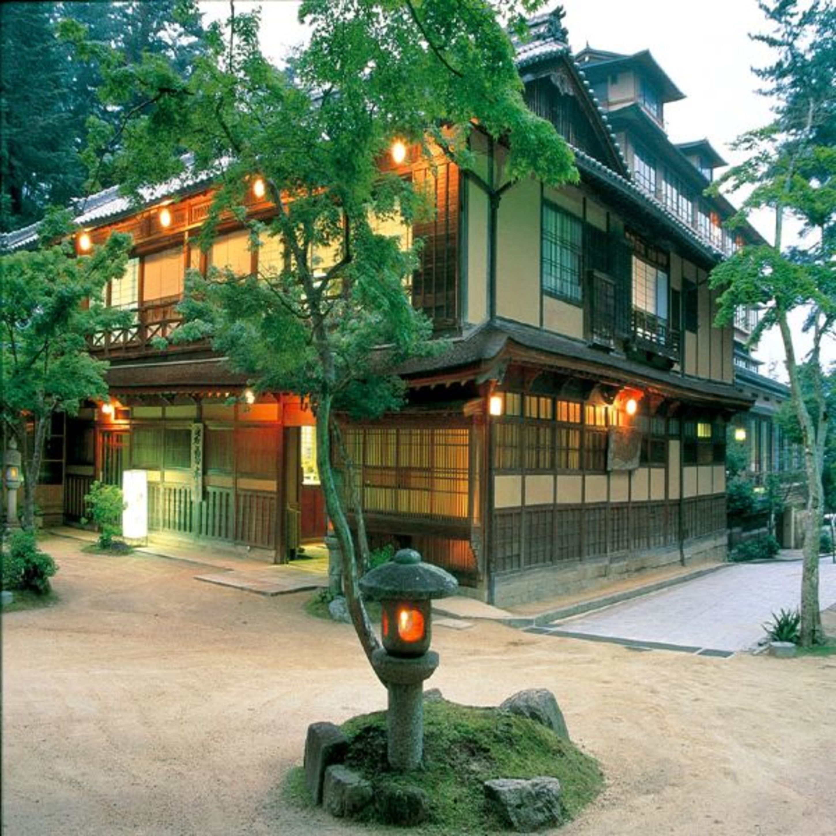 Un edificio japonés tradicional de varios niveles, con barandillas de madera y un jardín cuidado con un farol de piedra.