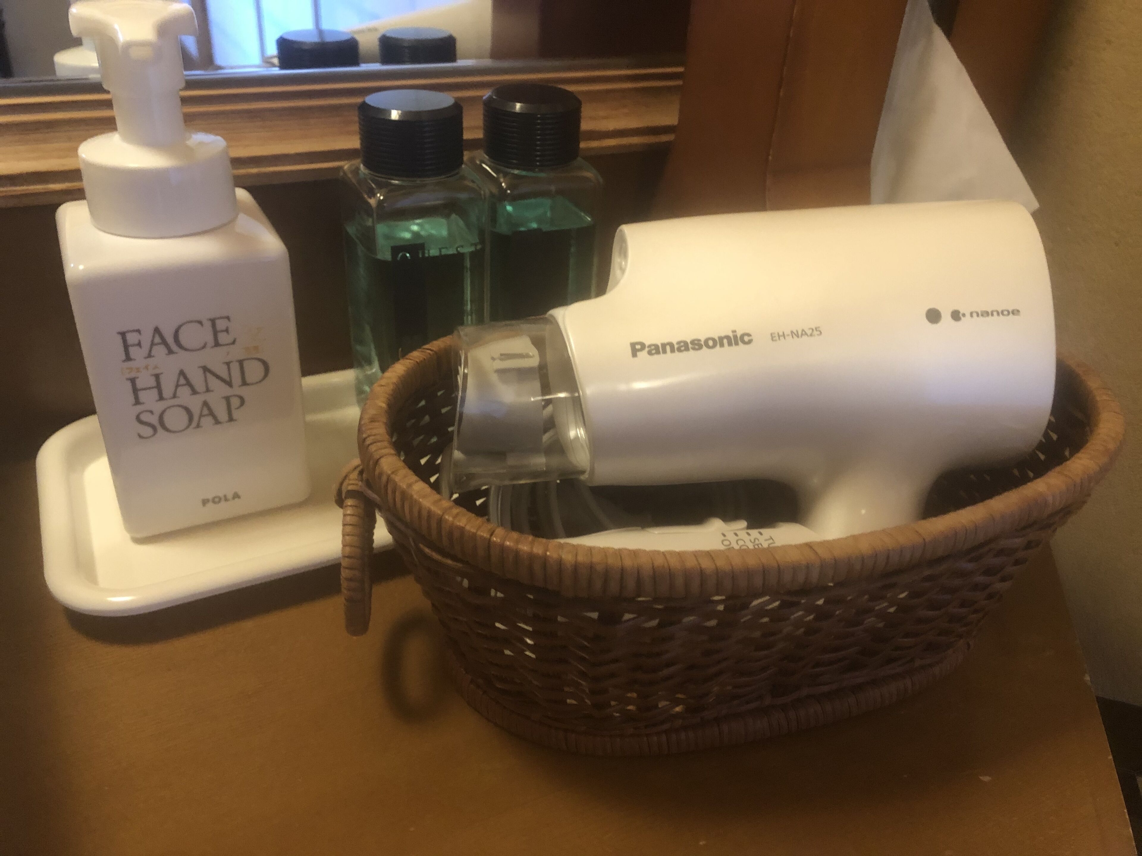 A bathroom counter with a bottle of face hand soap, two bottles of liquid soap, and a Panasonic hair dryer.
